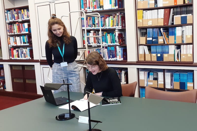 Two women consult journals in a library