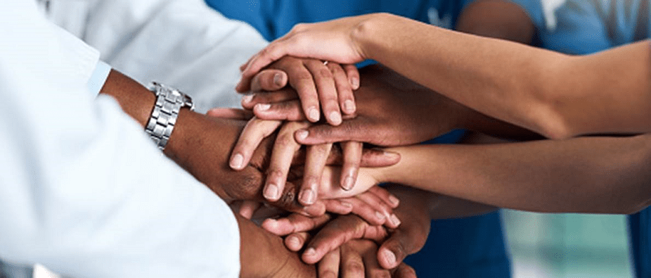 Hands all in, a group stands with their hands all piled on top of one another as an all in motion to support one another