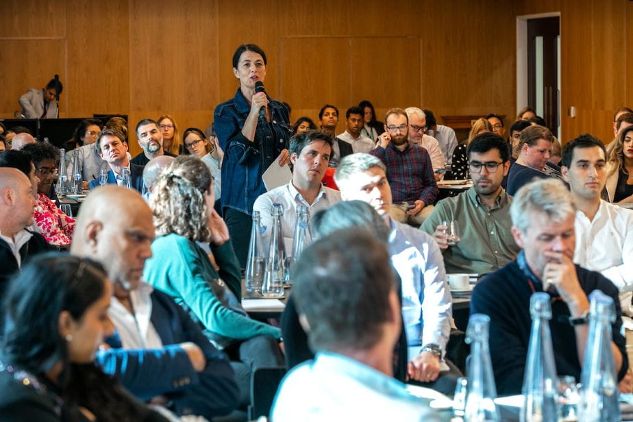 Woman speaking in microphone to crowd of people sitting at tables