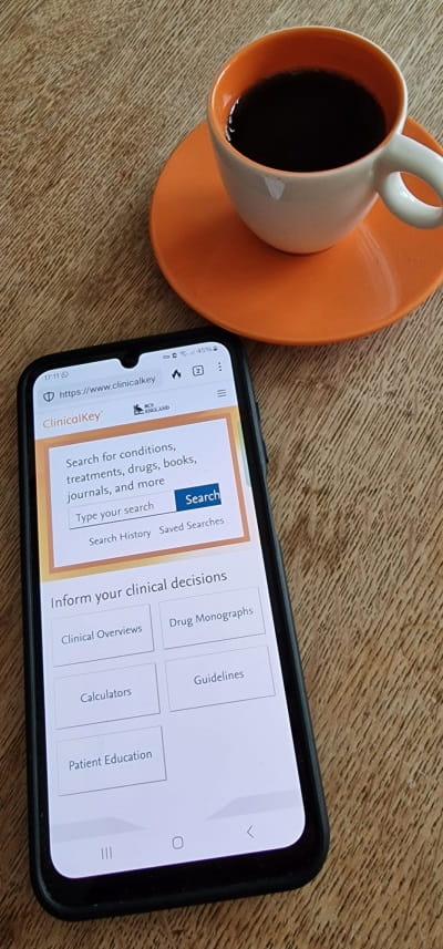 A smartphone showing the ClinicalKey homepage next to a cup of coffee