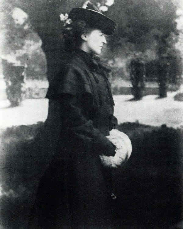 A black and white photograph of a woman in a coat and hat.