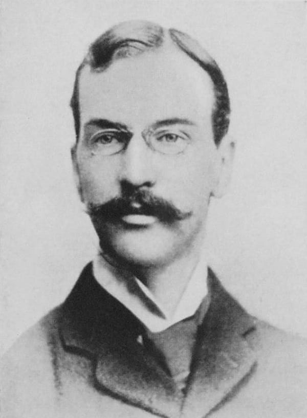 Black and white photograph of the head of a man with a pince-nez and a handlebar moustache