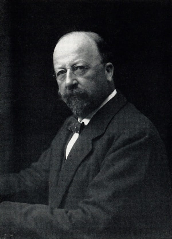 A black and white photograph of a man with a goatee and wire-rimmed spectacles