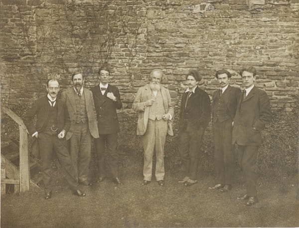 A sepia photograph of 7 men standing in front a wall