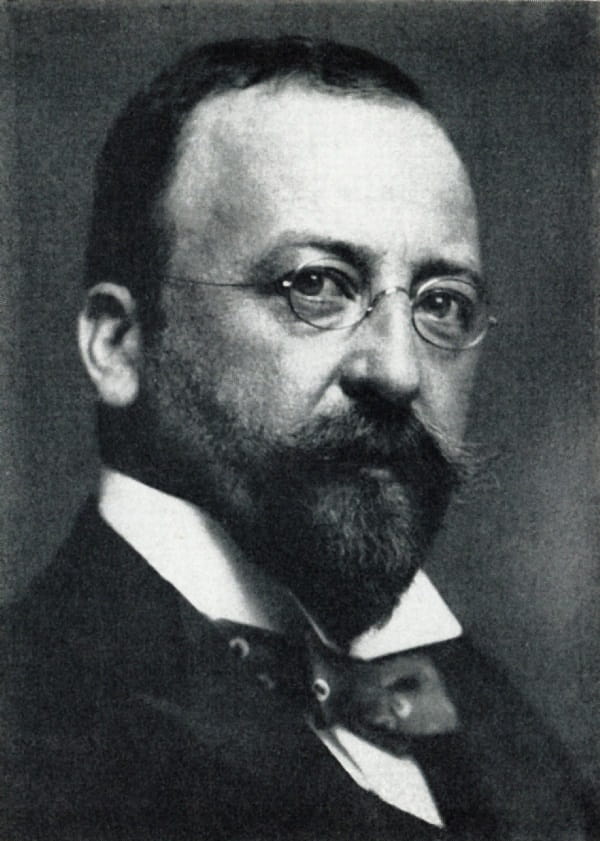 A black and white photograph of a man with a goatee and wire-rimmed spectacles